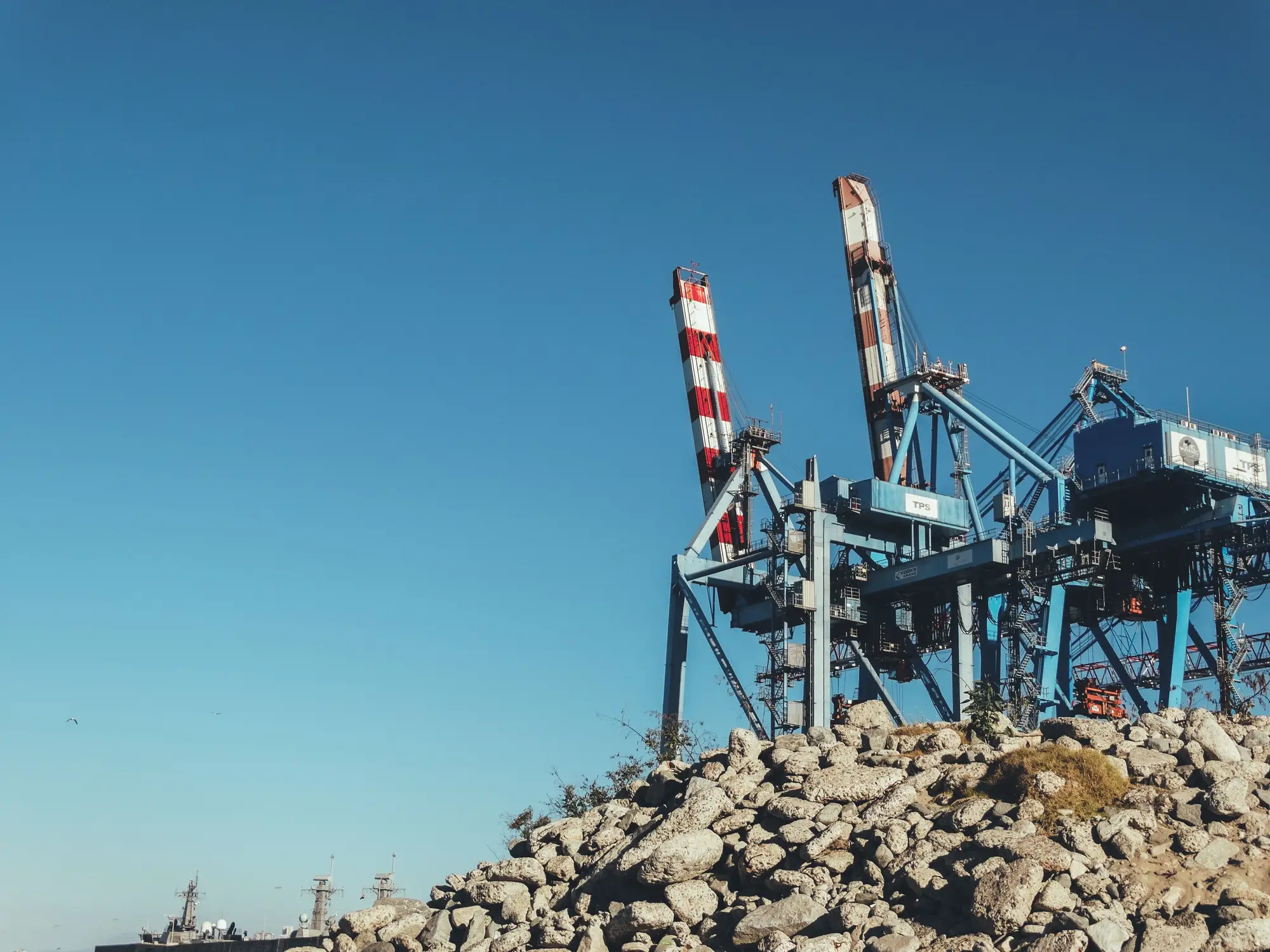 Two container cranes standing above a rock-armoured quay edge under a clear blue sky